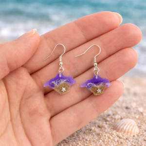 Handmade Isle of Wight purple resin earrings with real beach sand and starfish charm shown in hand for size
