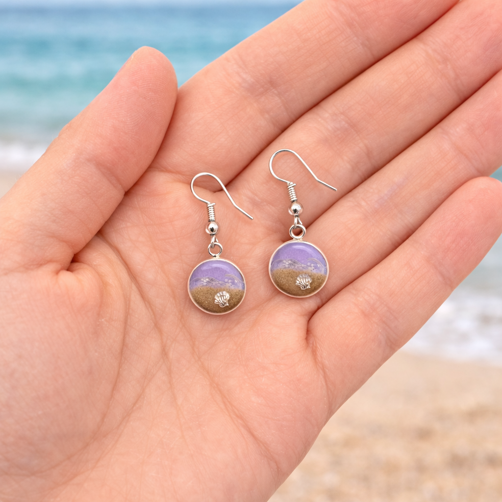 Purple resin beach earrings with sand and shell charm on silver hooks in hand to show scale