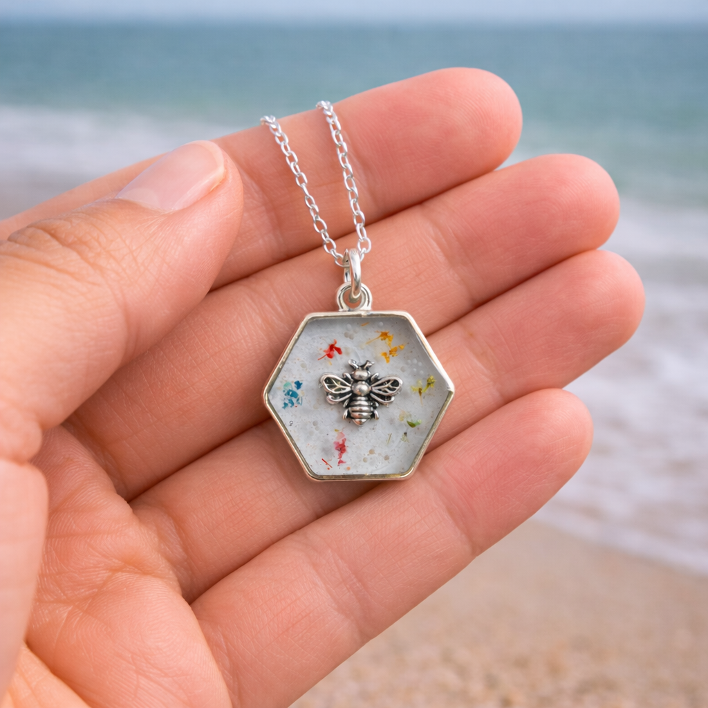 Hand holding a hexagon resin bee pendant necklace with pressed flowers showing the scale of the handmade jewellery piece.