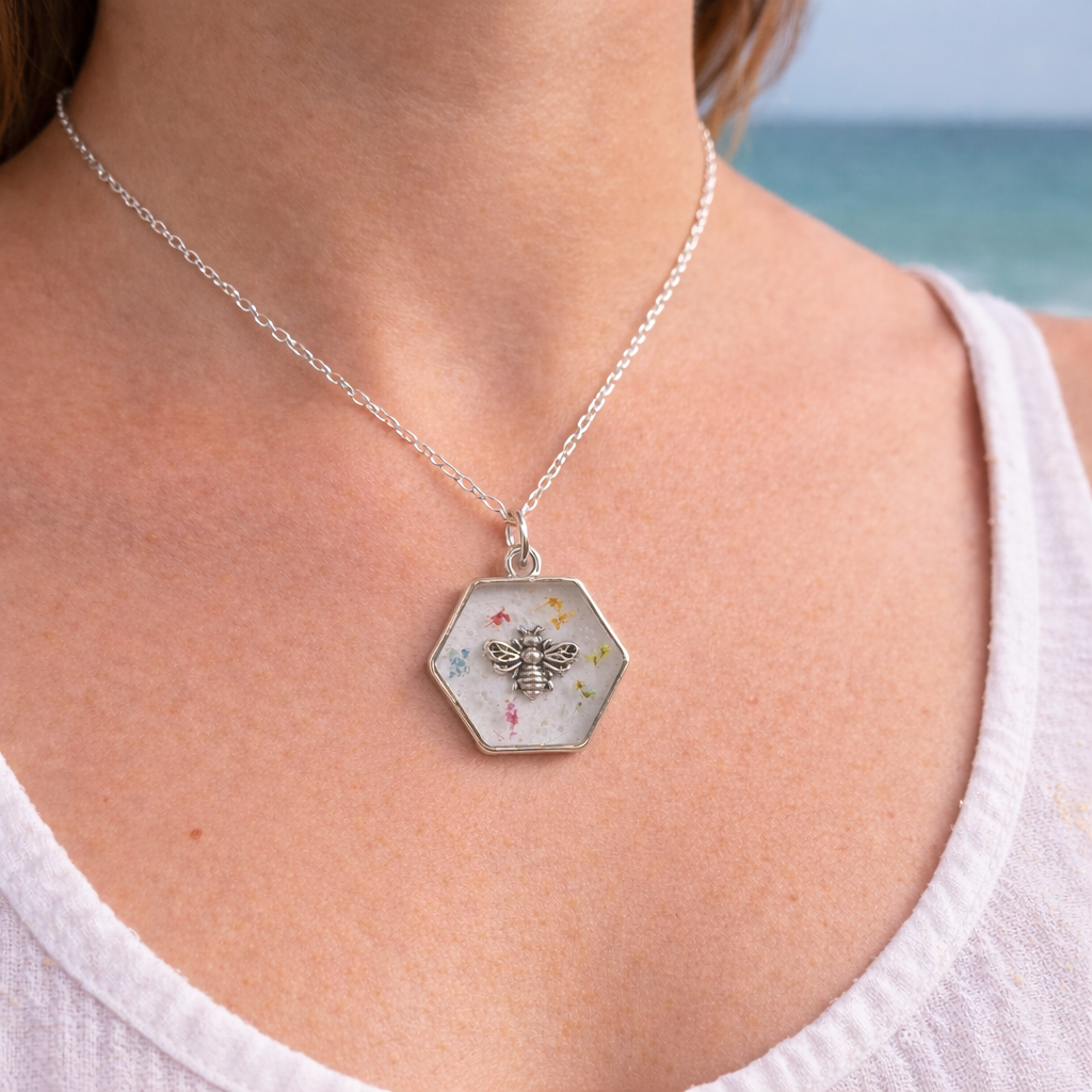 Woman wearing a handmade hexagon resin bee necklace with pressed flowers on a silver chain at the beach.