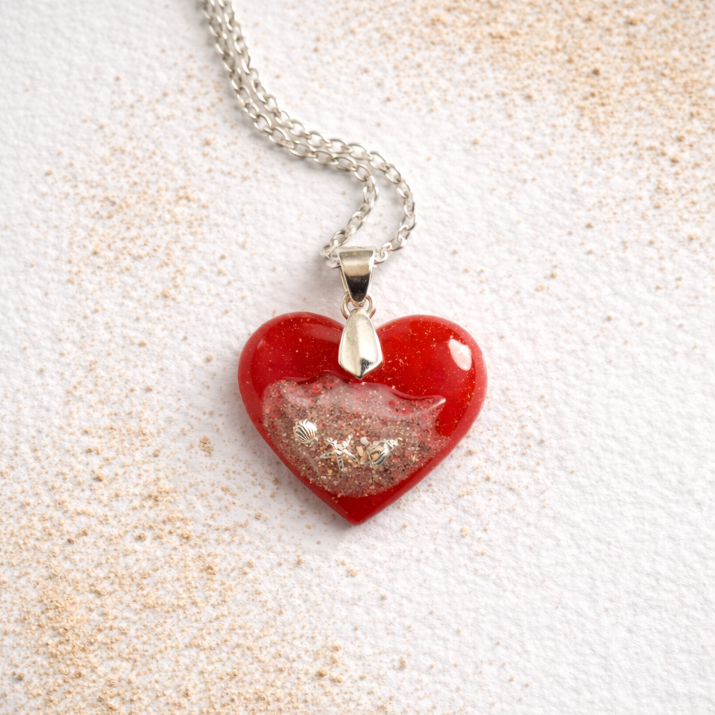 Handmade turquoise resin heart necklace with real Isle of Wight beach sand and silver seashell details on a soft white background with scattered sand.