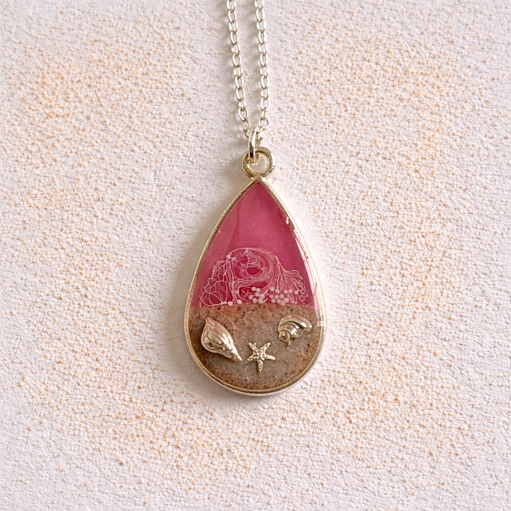Pink resin teardrop necklace with Isle of Wight sand and shell charms on silver chain.
