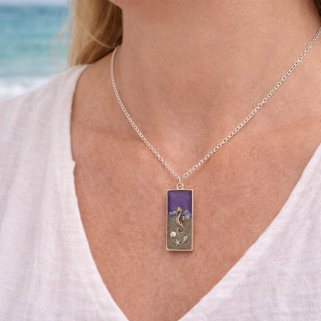 A woman wearing a purple resin seahorse necklace with Isle of Wight sand and shell charms on silver chain.