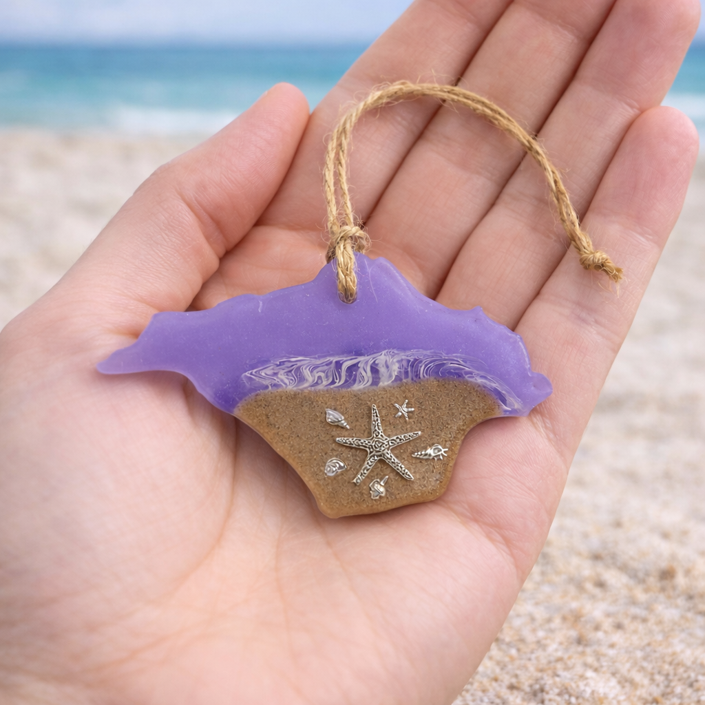 Handmade Isle of Wight shaped resin ornament with beach sand and silver starfish held in a hand to show scale.