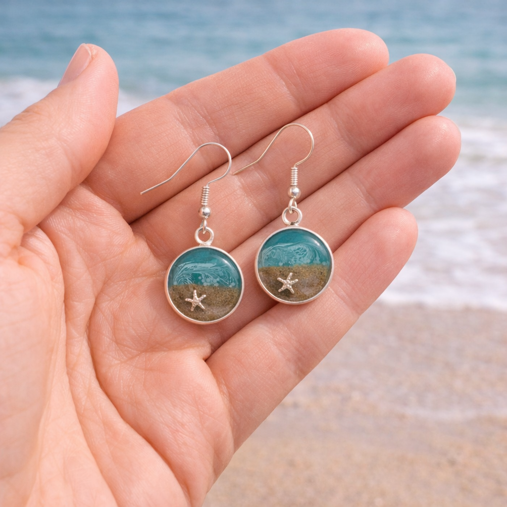 Turquoise resin beach earrings with sand and shell charm on silver hooks shown to scale in hand