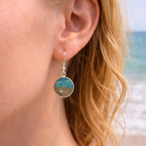 A woman wearing turquoise resin beach earrings with sand and shell charm on silver hooks