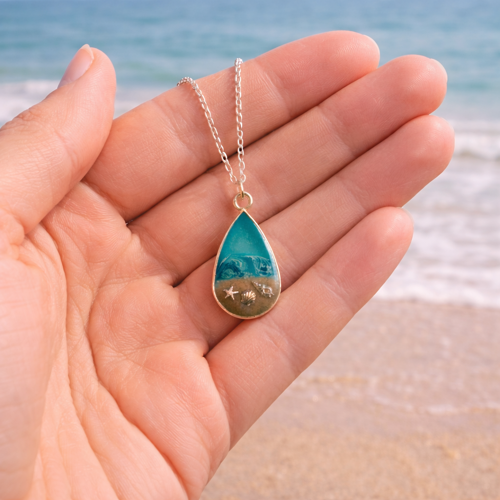 Turquoise resin teardrop necklace with Isle of Wight sand and shell charms on silver chain show in hand to scale