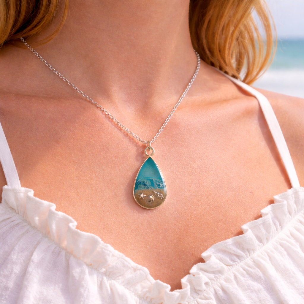A woman wearing a turquoise resin teardrop necklace with Isle of Wight sand and shell charms on silver chain.