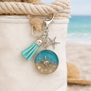 Isle of Wight resin keyring with real beach sand, starfish charm, and turquoise tassel shown on beach bag.