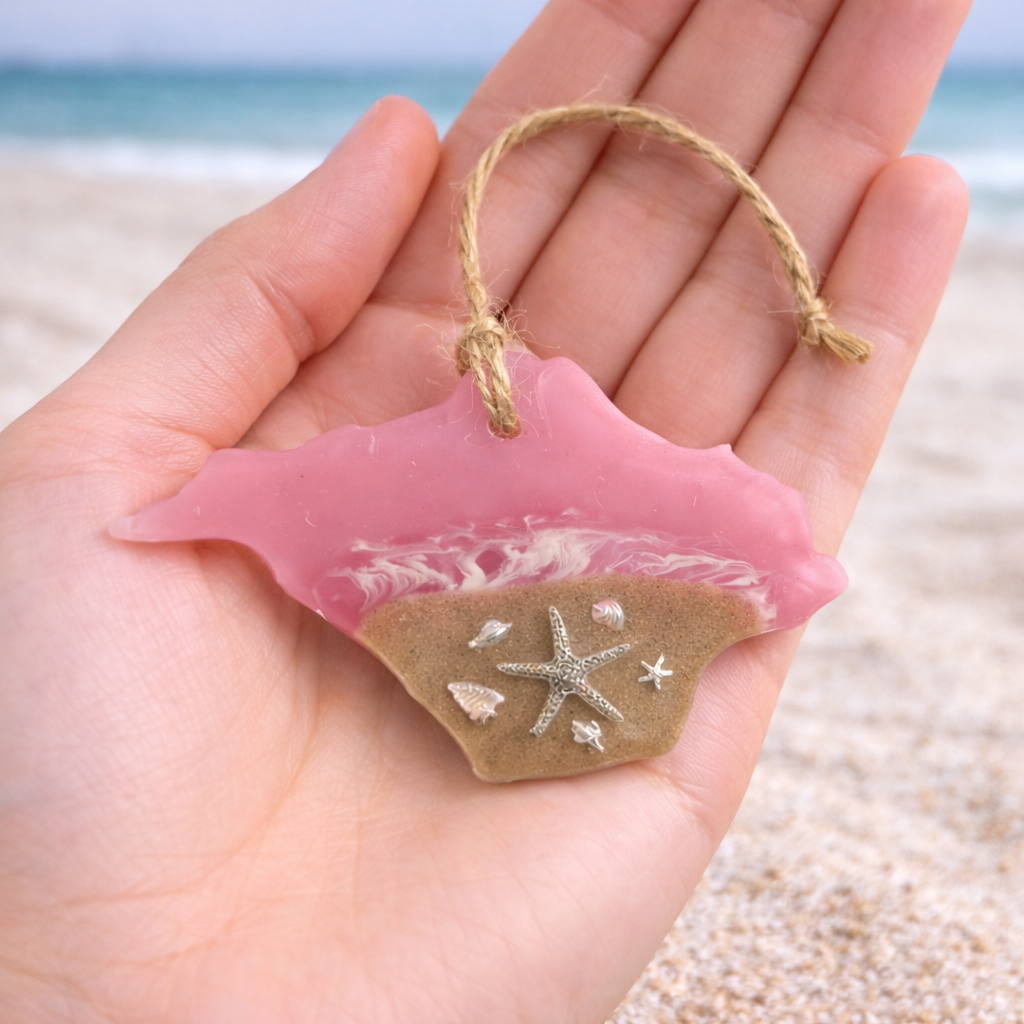 Handmade Isle of Wight shaped resin ornament with beach sand and silver starfish held in a hand to show scale.