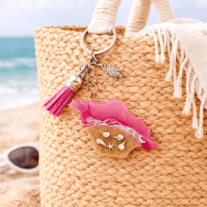 Isle of Wight pink resin keyring attached to a woven beach bag on sandy beach with sea in the background