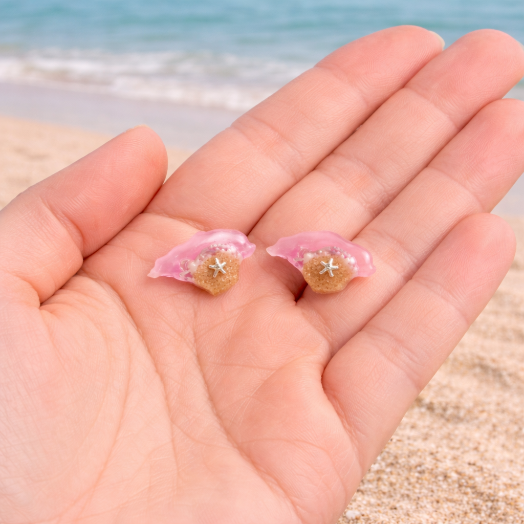 Isle of Wight resin stud earrings shown in hand for size with beach background and pink sea design