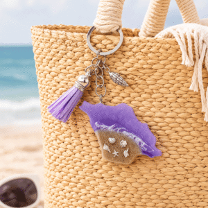 Isle of Wight purple resin keyring attached to a woven beach bag on sandy beach with sea in the background